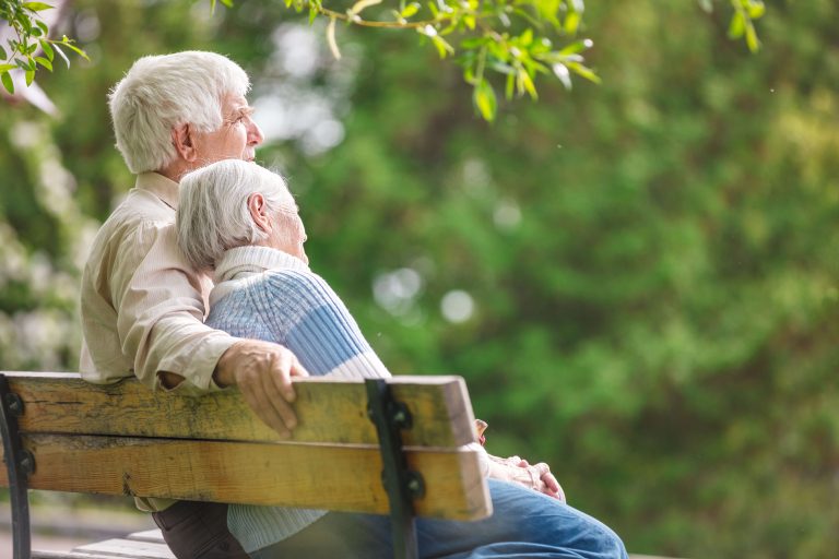 Compass Associates - elderly couple sat on a bench leant into each other surrounded by greenery