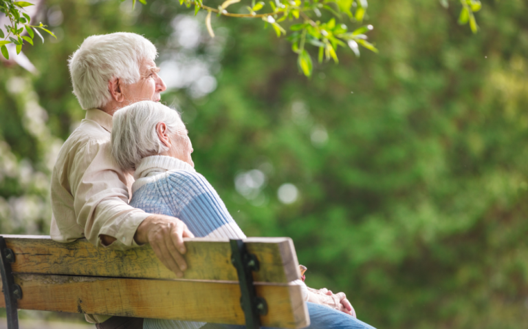 Compass Associates - Elderly couple sat on an outdoor bench, cuddled together and looking out to the scenic greenery views around