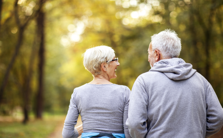 Compass Associates - elderly couple looking at each other and holding hands with their backs to the camera, walking in a park/green area