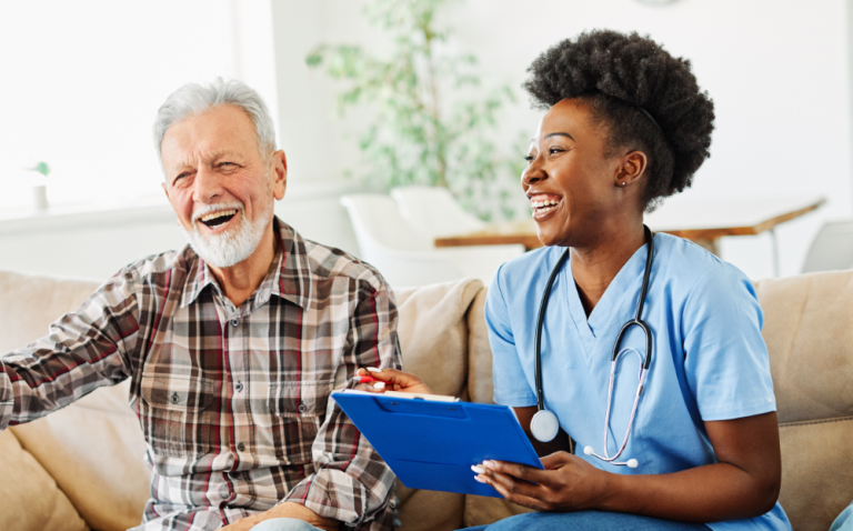 Compass Associates - elderly man sat on a sofa speaking to a healthcare professional with both of them smiling and laughing