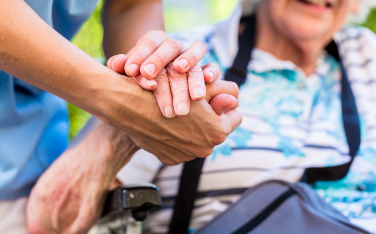 Compass Associates - Elderly person sat in a wheelchair holding the hand of a social care professional
