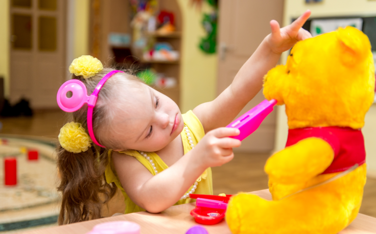 Compass Associates - A young girl in a playroom playing with a Winnie the Pooh bear and toys that look like doctor