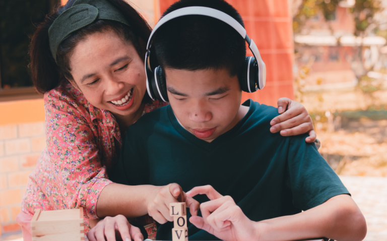 Compass Associates - Person providing support and comfort for a young person with a learning disability who is wearing headphones and focusing on some small blocks covered in letters
