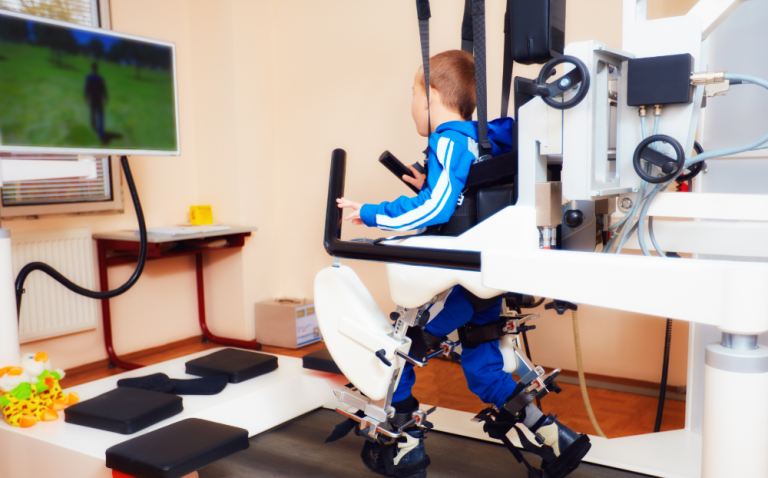 Compass Associates - young boy strapped in a mobility machine, looking at a screen of someone walking to aid him in learning to walk and gain strength