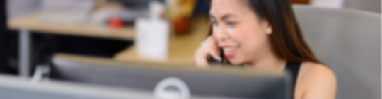 Compass Associates - Contact Us - blurred, candid image of consultant behind a computer screen whilst on the phone talking and smiling
