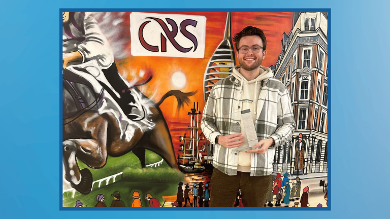 Compass Associates - Employee of the Quarter - Rory Birch Employee of the Quarter - Rory is holding his trophy and stood in front of the Manchester office mural featuringn Spinaker Tower and horse riding paintings on the wall